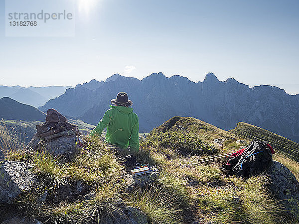 Italien  Lombardei  Bergamaskische Voralpen  Wanderer sitzt auf dem Aussichtspunkt des Monte Gardena  Cima Bagozza gegen die Sonne