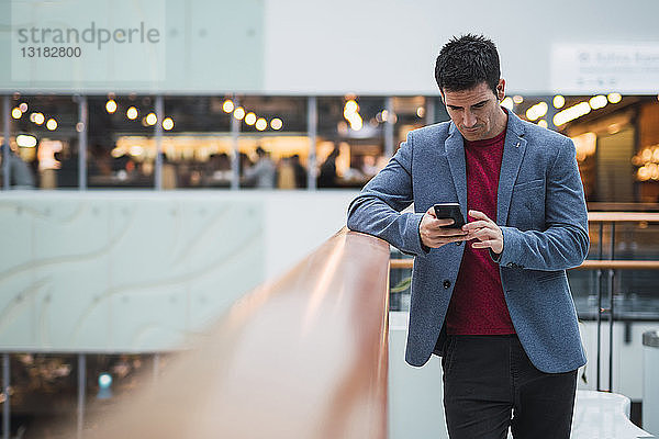 Geschäftsmann in der Lobby eines modernen Gebäudes  mit Smartphone