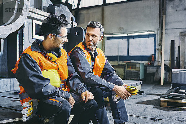 Zwei Männer in Arbeitsschutzkleidung unterhalten sich während der Pause in der Fabrik