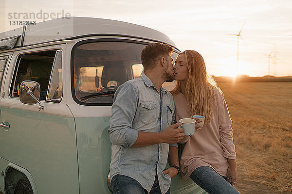 Junges Paar küsst sich am Wohnmobil in ländlicher Landschaft
