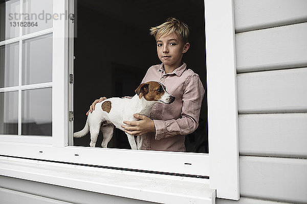 Porträt eines Jungen mit Jack Russel Terrier  der aus dem offenen Fenster schaut