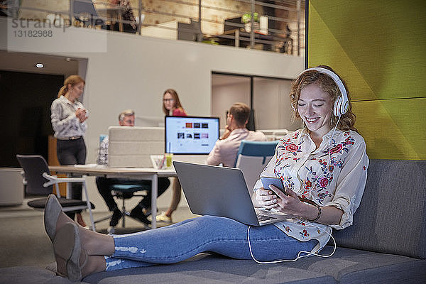 Junge Frau  die in einem modernen Kreativbüro arbeitet  benutzt Laptop und Kopfhörer