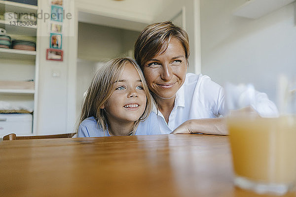 Lächelnde Mutter und Tochter sitzen zu Hause am Küchentisch