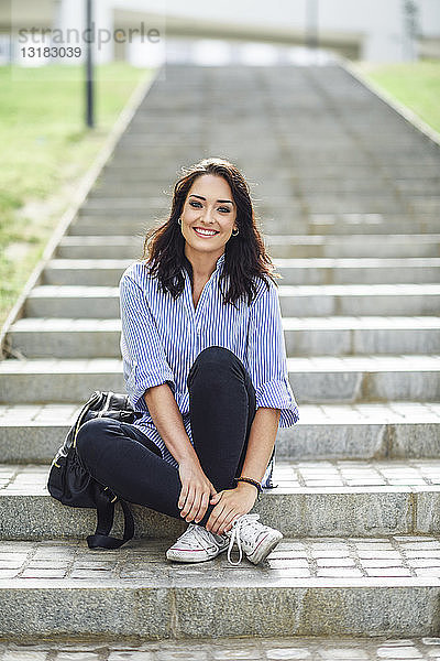 Porträt eines lächelnden Studenten  der auf einer Treppe im Freien sitzt
