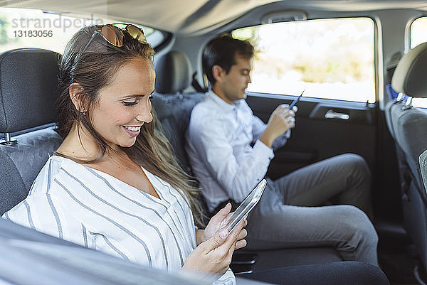 Frau und Mann benutzen Tablet und Handy auf dem Rücksitz eines Autos