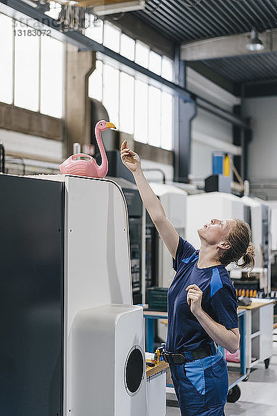 Junge Frau  die als Facharbeiterin in einem High-Tech-Unternehmen arbeitet und mit einem rosa Flamingo spielt