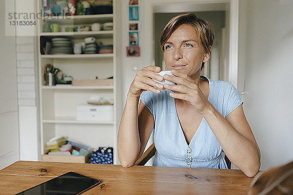 Frau sitzt zu Hause am Tisch mit einer Tasse Kaffee
