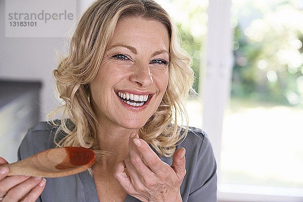 Porträt einer glücklichen Frau  die Tomatensauce vom Kochlöffel probiert