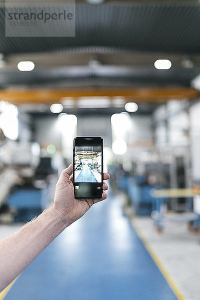 Smartphone in der Hand haltend in einer Fabrikhalle