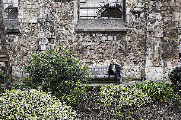 UK  London  älterer Geschäftsmann sitzt auf einer Bank in einem Innenhof und entspannt