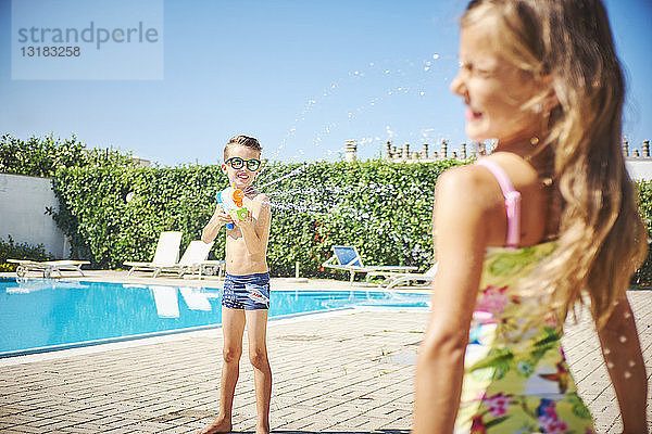 Junge mit Wasserpistole spritzt auf Mädchen am Pool