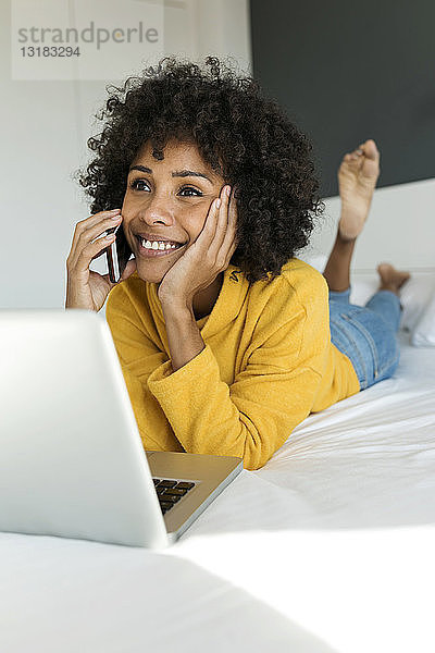 Lächelnde Frau liegt im Bett und telefoniert mit dem Handy