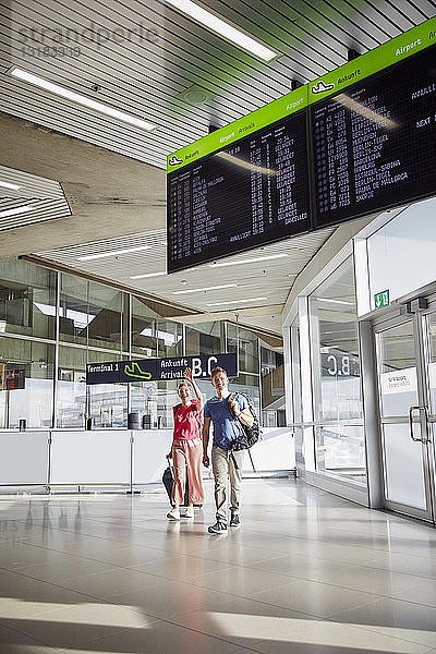 Glückliches Paar geht am Flughafen mit winkender Frau