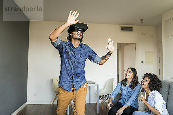 Zwei Frauen beobachten Mann mit VR-Brille zu Hause