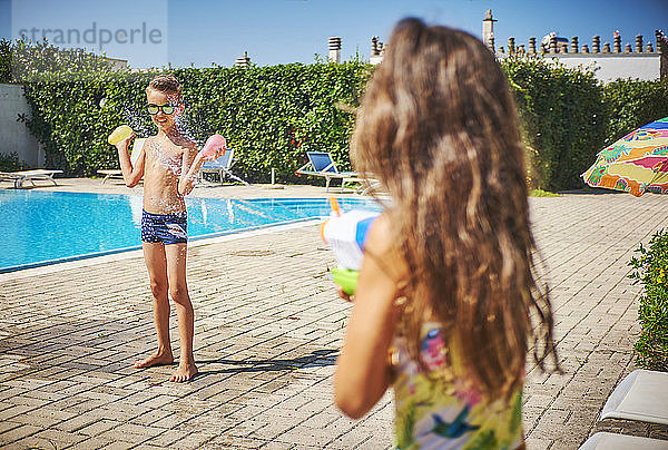 Mädchen mit Wasserpistole spritzt auf Jungen  der Wasserbomben am Beckenrand hält