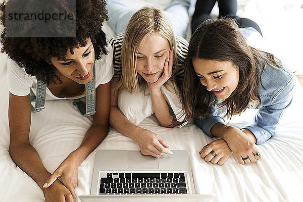 Drei Freundinnen liegen im Bett und teilen sich einen Laptop