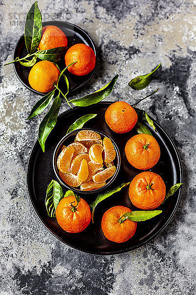 Mandarinen mit Blättern  auf Teller und Stücke in Schale