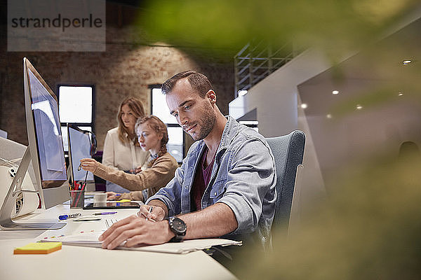 Mann arbeitet am Schreibtisch im Büro und lächelt