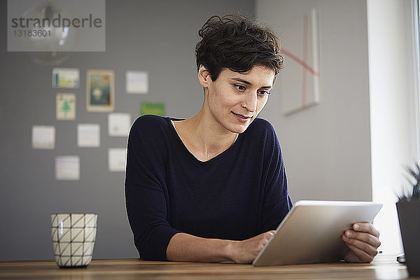 Frau sitzt zu Hause am Tisch mit Tablette