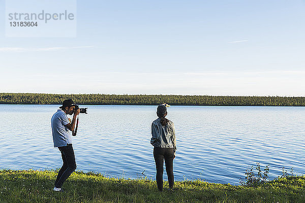 Junger Mann fotografiert junge Frau an einem See