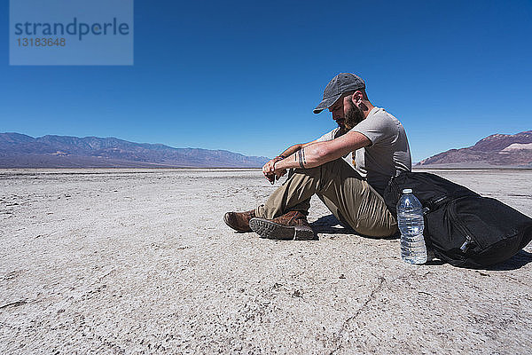 USA  Kalifornien  Death Valley  Mann sitzt am Boden in der Wüste und ruht sich aus