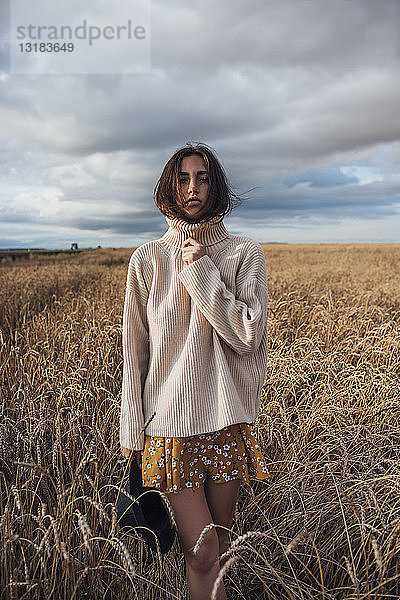 Porträt einer jungen Frau mit übergroßem Rollkragenpullover im Maisfeld stehend
