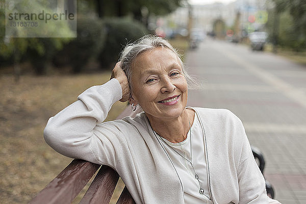 Porträt einer lächelnden älteren Frau  die sich auf einer Bank entspannt