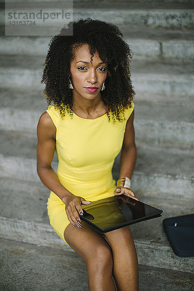 Porträt einer modischen Geschäftsfrau in gelbem Kleid auf einer Treppe sitzend mit digitalem Tablett
