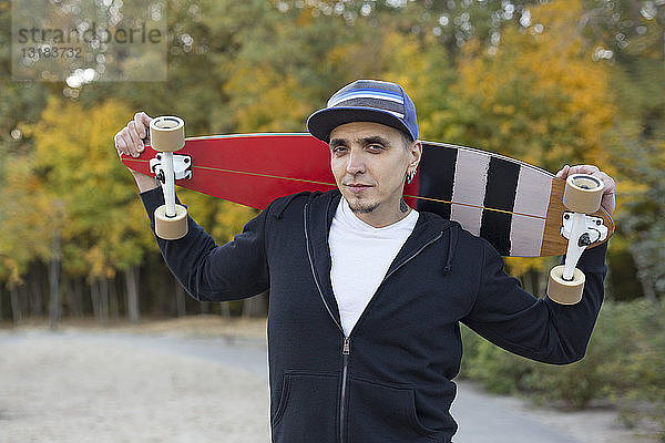Porträt eines Mannes mit Skateboard auf den Schultern im Herbst