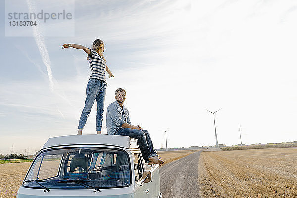 Glückliches Paar auf dem Dach eines Wohnmobils in ländlicher Landschaft