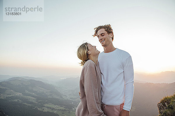 Schweiz  Grosse Mythen  glückliches junges Paar steht bei Sonnenaufgang in der Berglandschaft