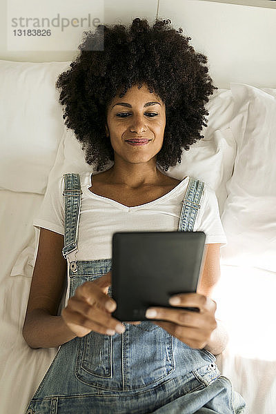 Lächelnde Frau liegt im Bett und liest E-Book
