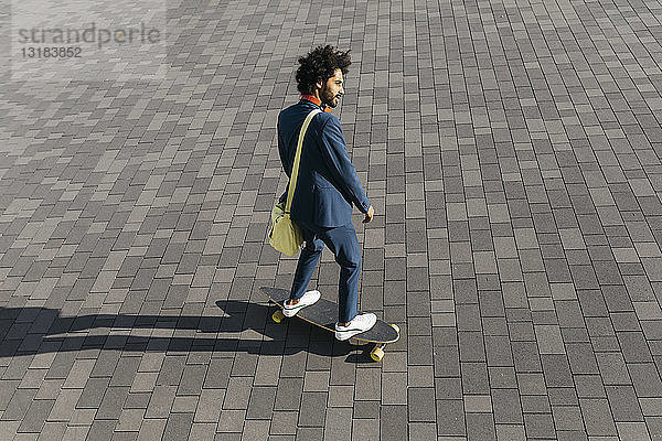 Junger Geschäftsmann fährt Skateboard auf einem Platz