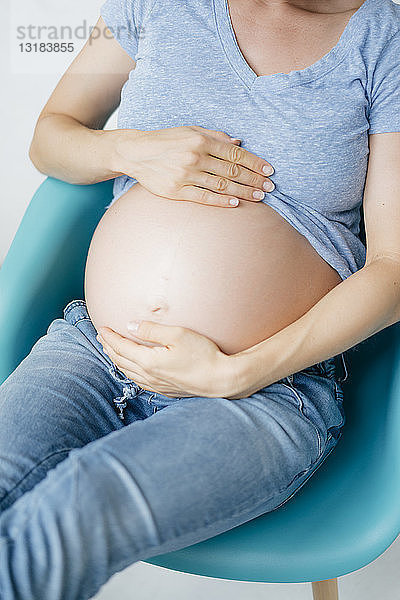 Nahaufnahme des Bauches einer schwangeren Frau  die auf einem Stuhl sitzt