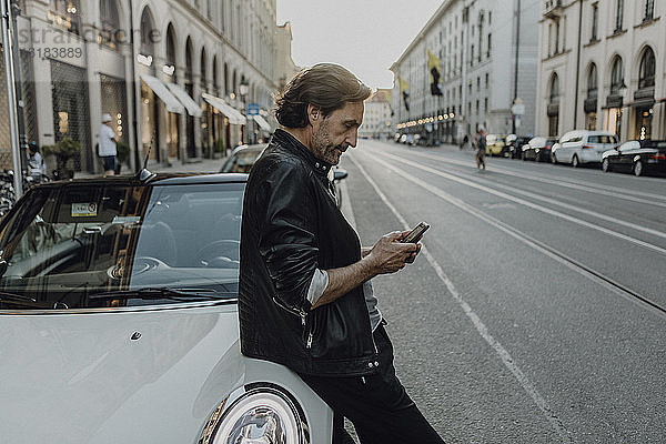 Reifer Mann lehnt sich an Auto an und hält Smartphone  München  Bayern  Deutschland