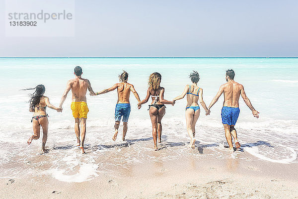 Gruppe von Freunden am Strand  rennt ins Meer und hält sich an den Händen