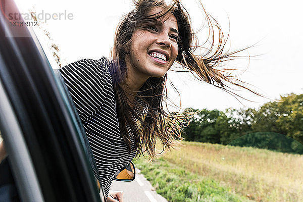Glückliche junge Frau lehnt sich aus dem Autofenster