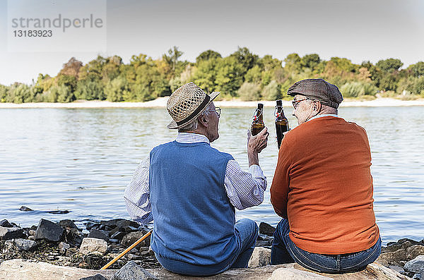 Alte Freunde sitzen am Flussufer und trinken Bier