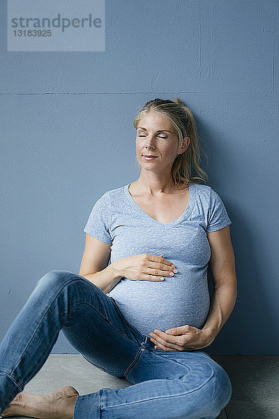 Porträt einer lächelnden schwangeren Frau  die mit geschlossenen Augen auf dem Boden sitzt