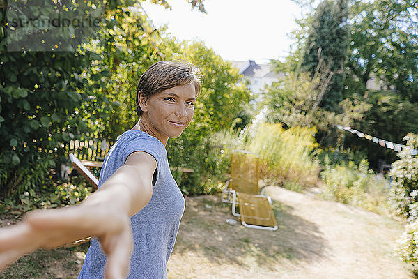 Porträt einer lächelnden Frau im Garten  die die Hand ausstreckt