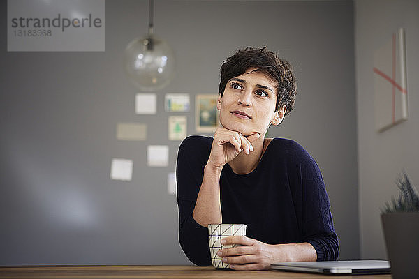 Porträt einer Frau zu Hause am Tisch sitzend bei einer Tasse Kaffee