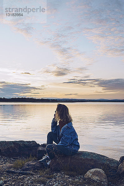 Junge Frau sitzt am Inari-See und schaut auf Aussicht  Finnland