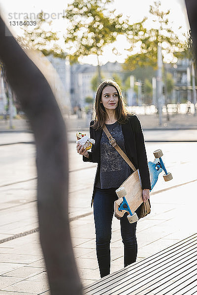 Junge Frau mit Longboard in der Stadt in Bewegung