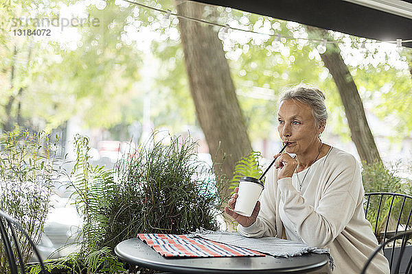 Ältere Frau mit einem Getränk in einem Außencafé