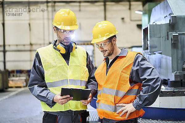 Zwei Männer in Arbeitsschutzkleidung halten Klemmbrett und unterhalten sich in der Fabrik