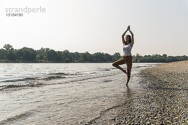Junge Frau  die im Wasser eines Flusses steht und Yoga praktiziert