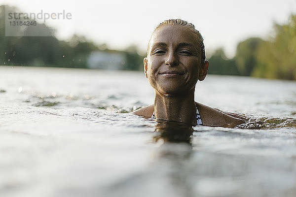Porträt einer lächelnden Frau  die in einem See schwimmt