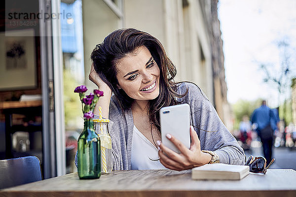 Glückliche Frau schaut auf Handy im Außencafé