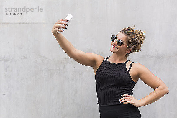 Porträt einer lächelnden  schwarz gekleideten jungen Frau  die sich mit einem Smartphone selbstständig macht