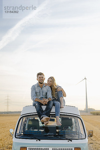 Porträt eines glücklichen jungen Paares auf dem Dach eines Wohnmobils in ländlicher Landschaft